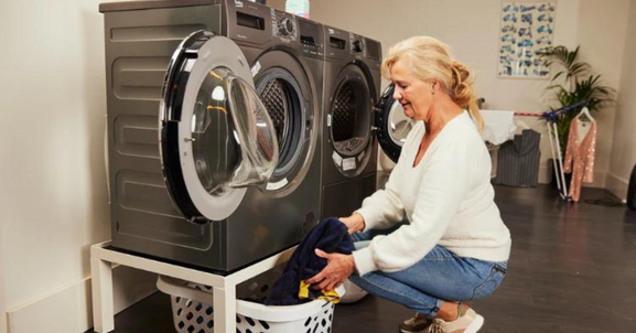 vrouw pakt de was in de wasmachine die op een wasmachine verhoger staat